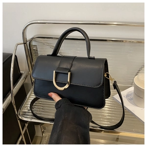 Dettaglio di una borsa in pelle nera con fibbia dorata su un supporto moderno