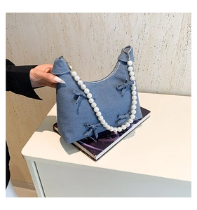 Detail of blue denim hobo bag featuring decorative bows and a white pearl handle