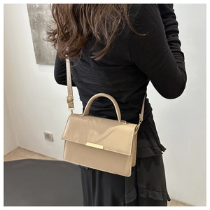 Detail of a beige minimalist handbag with gold metal bar accent on a female model
