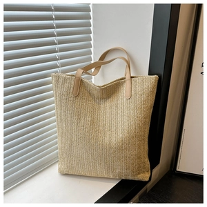 Detail view of straw tote bag with herringbone weave and slim brown leather handles