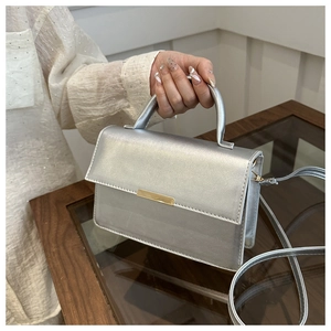 Detail of silver metallic handbag with gold hardware and reinforced handle on a white dress