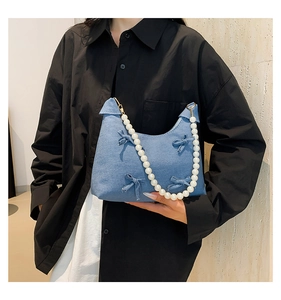Detail of blue denim shoulder bag featuring pearl strap and bow decorations