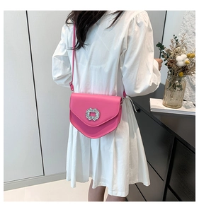 Détail du sac de selle rose vif avec boucle en strass porté sur une robe blanche