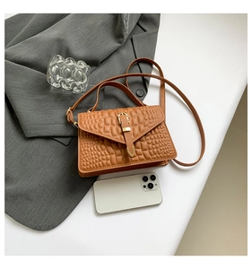 Detail of brown crocodile pattern shoulder bag with gold clasp on a white surface
