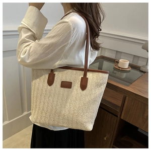 Detail of woven straw tote bag with V-shaped pattern and dark brown leather handles