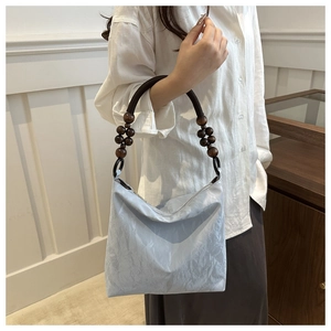 Detail of light blue wrinkled fabric handbag with braided rope handle and wooden beads