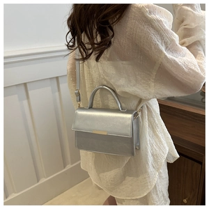 Rear view of a silver metallic crossbody bag worn by a model in a minimalist room