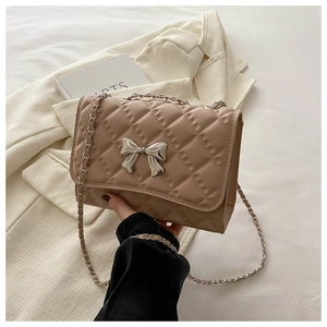 Detail of khaki quilted crossbody bag with silver bow clasp and chain strap on blazer