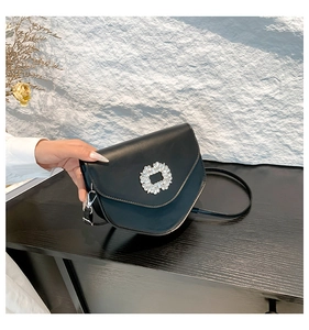 Gros plan d'un sac bandoulière noir avec boucle ronde en strass et détails de crochet métal