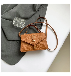 Close-up of brown croc-embossed texture and golden buckle on an envelope handbag