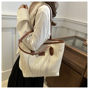 Detail of straw tote bag with brown faux leather handles worn by a female model
