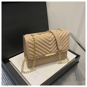 Detail of beige quilted flap bag with V-shaped chevron stitching and gold chain strap