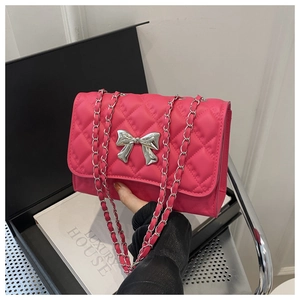 Detail of rose pink quilted crossbody bag featuring silver bow accent and chain strap