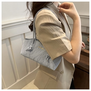Détail du sac cabas plissé bleu clair avec bandoulière nouée et logo doré sur blazer