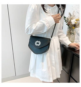 Détail d'un sac selle noir élégant avec boucle en cristal porté sur une robe blanche