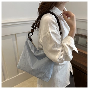 Detailed view of light blue pleated shoulder bag with dark brown beaded handle strap