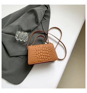 Detail of caramel crocodile pattern handbag placed on a grey blazer for workwear style