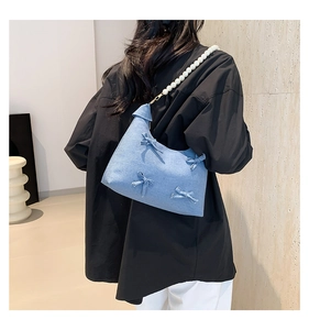 Detail of light blue denim shoulder bag with ribbon bows and white pearl strap