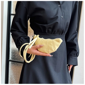 Detail of pale yellow croissant bag with elegant pleats held against black dress