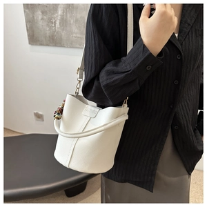Detailed shot of white litchi pattern bucket bag with FASHION embossed logo and silk scarf