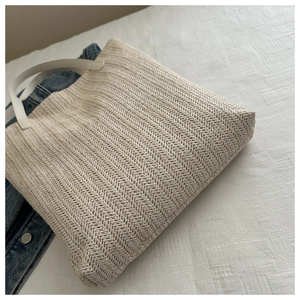Detailed view of the straw weave texture and white faux leather handle of the tote bag