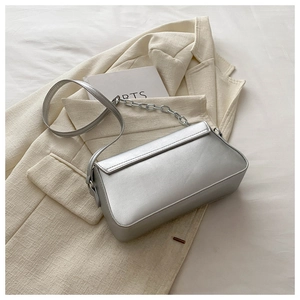 Detail of silver metallic handbag flap with leather and chain strap on a white blazer