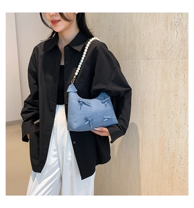 Detail of light blue denim shoulder bag with decorative bows and white pearl strap