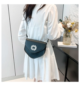 Détail du sac selle noir avec boucle en strass sur une robe blanche