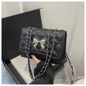 Close-up of black quilted shoulder bag with silver bow buckle and metal chain strap