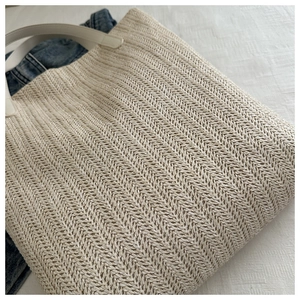 Macro view of beige herringbone straw weave and white leather handle on a summer tote bag