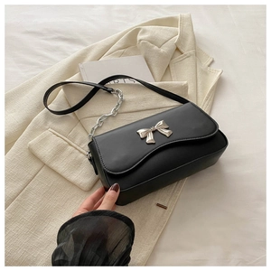 Close-up of black matte shoulder bag with silver butterfly buckle on textured beige blazer