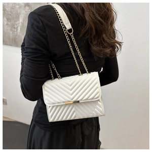 Detail of white V-quilted shoulder bag with gold chain strap worn by a model