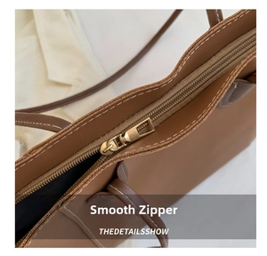 Detail shot of smooth gold-tone zipper and white stitching on brown tote bag