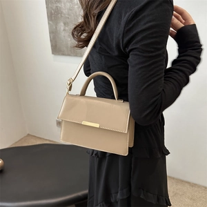 Chic beige crossbody bag with top handle and gold clasp on a model in black dress