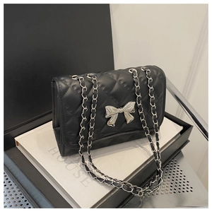 Close-up of quilted leather texture and silver bow buckle on the black chain bag