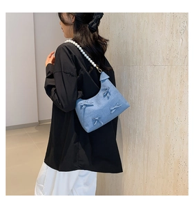 Detail of light blue denim shoulder bag with ribbon bows and white pearl strap