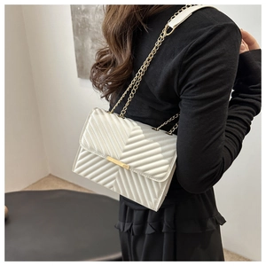 Detail of white V-quilted shoulder bag with gold chain strap and metal bar closure