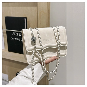 Detail of cream crossbody bag with wavy flap, gold chain and textured metal ball slider