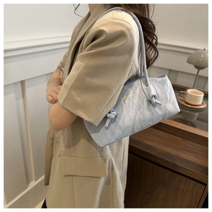 Détail du sac à bandoulière bleu clair à texture plissée avec logo doré et nœud