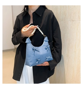 Detail of blue denim handbag featuring large pearl handle and cute ribbon bow accents