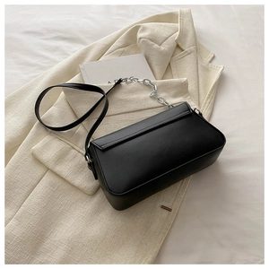 Detail of black matte leather baguette bag with silver chain and crossbody strap