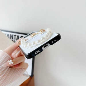 Detail of white leather Z Flip 6 case with gold ring and elegant cream pearl wrist strap