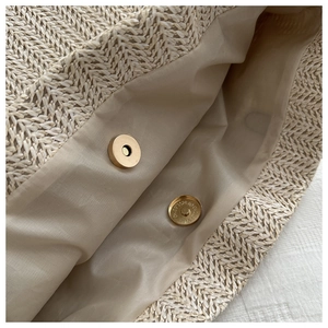 Detail of golden magnetic snap button closure on straw woven bucket bag with beige lining
