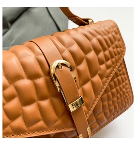 Close-up of caramel faux leather bag featuring 3D waffle texture and gold buckle