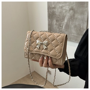 Detail of beige quilted crossbody bag with silver bow clasp and metal chain strap