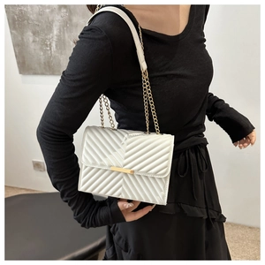 Detailed view of white quilted crossbody bag with gold chain strap and lock on a model