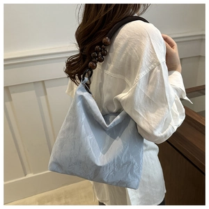 Detail of light blue pleated velvet shoulder bag featuring unique wooden bead strap