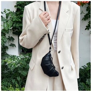 Close-up of a mini black leather croissant neck bag on a beige blazer outfit