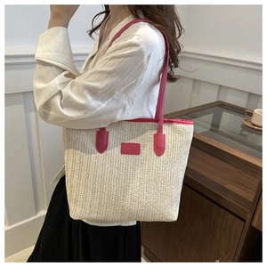 Detail of woven straw tote bag featuring contrast pink leather handles for summer beach style