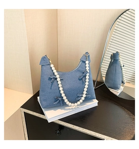 Detail of light blue denim tote with bow accents and elegant white pearl shoulder strap